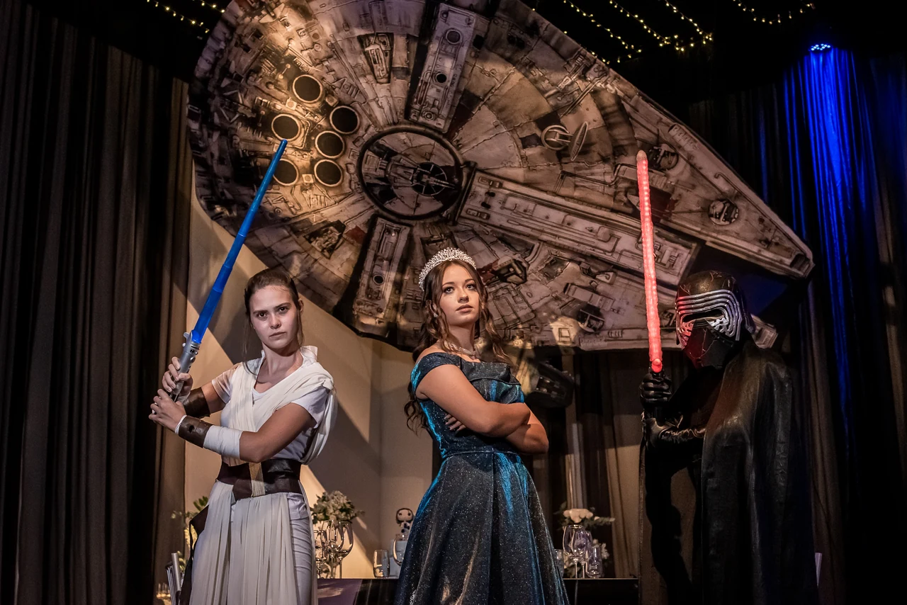 Debutante acompanhada por personagens no cenário de sua festa temática de 15 anos.