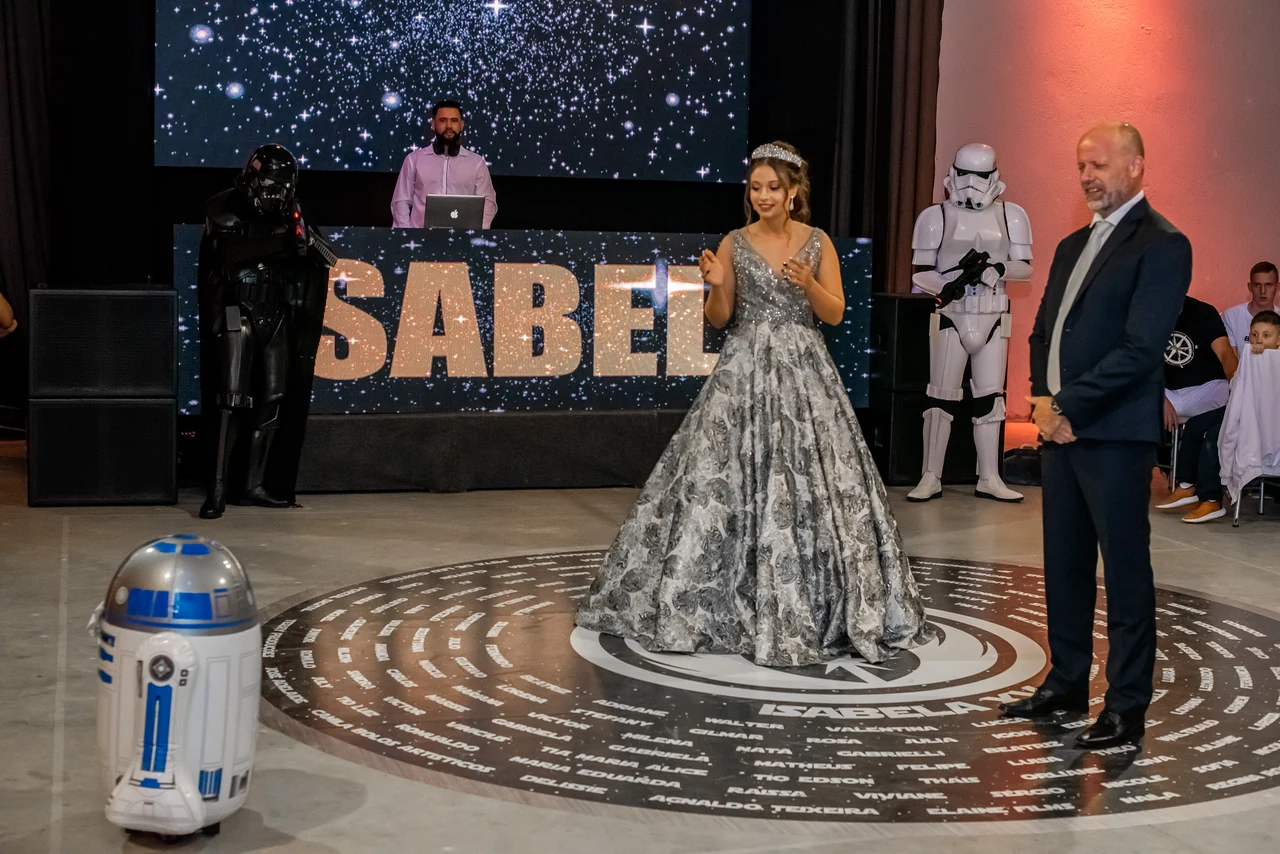 Debutante acompanhada por um familiar diante do telão durante a celebração de 15 anos.